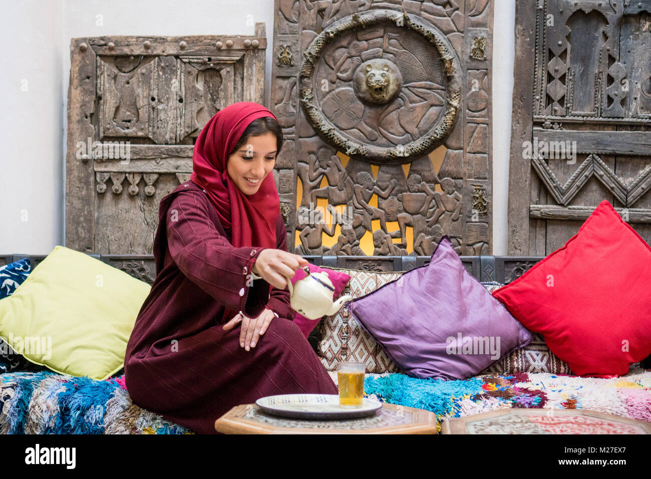 La donna araba nel tradizionale rosso abbigliamento con il hijab sul suo capo bere un tè tradizionale in medio ambiente orientale Foto Stock
