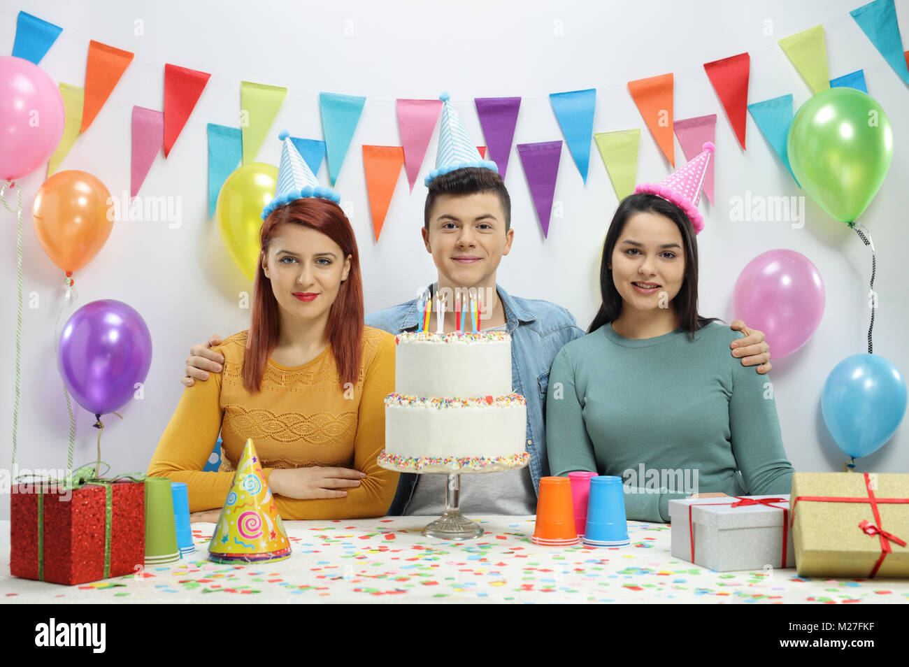 Gli adolescenti con party cappelli e una torta di compleanno contro una parete con decorazioni Foto Stock