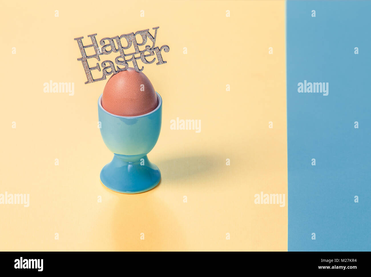 Gilttery Felice Pasqua sulla parte superiore dell'uovo sodo in pastello blu cup su carta normale sfondo Foto Stock