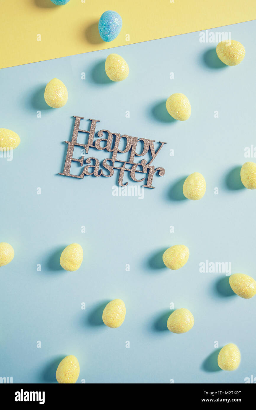 Felice Pasqua design con i colori giallo e blu glittery uova di pasqua su carta. Il minimo di colore pastello concetto nel raccolto verticale Foto Stock