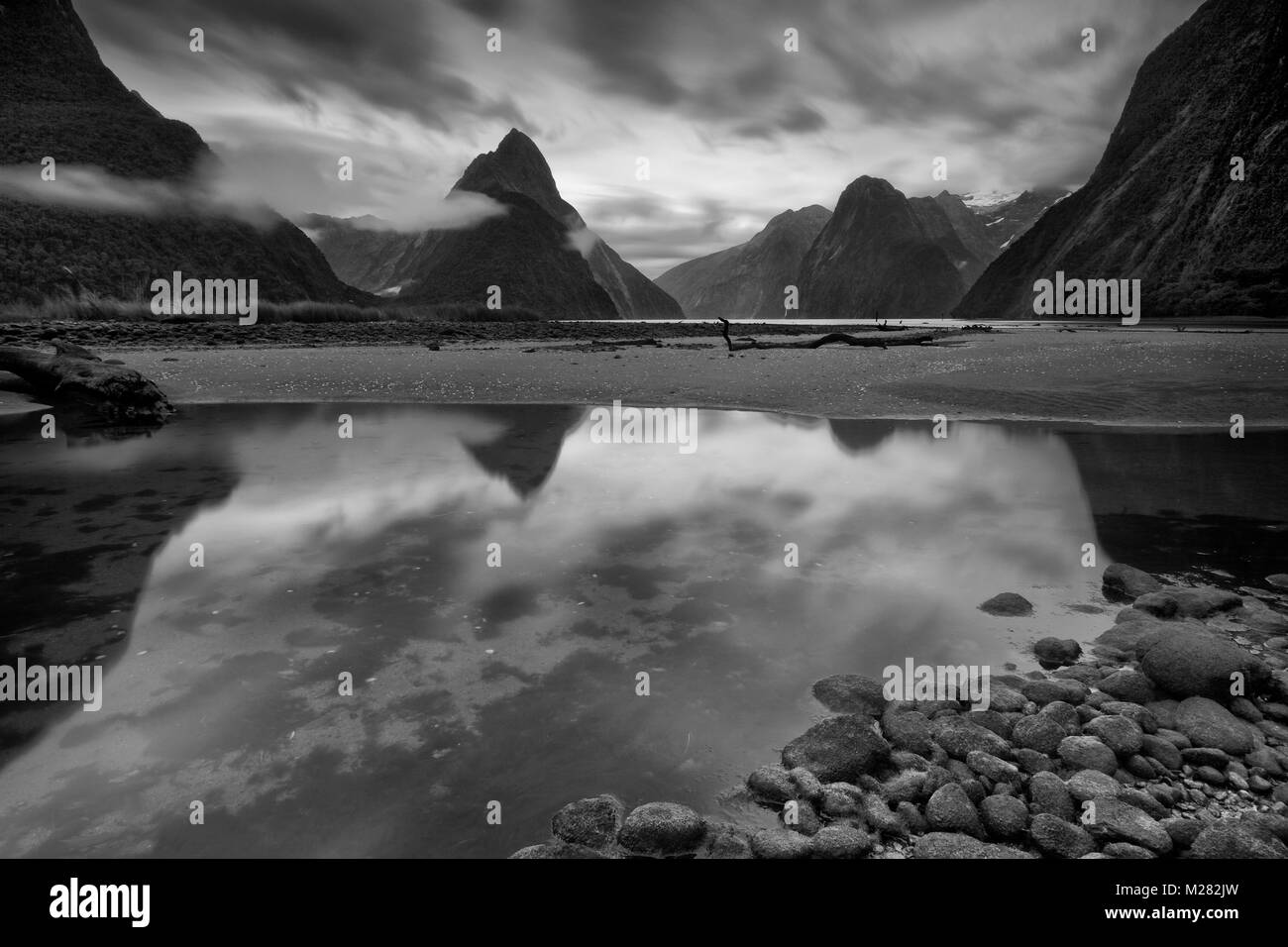 Gli alti picchi di Milford Sound riflettono in acqua ancora di questo moody in bianco e nero lunga esposizione. Foto Stock