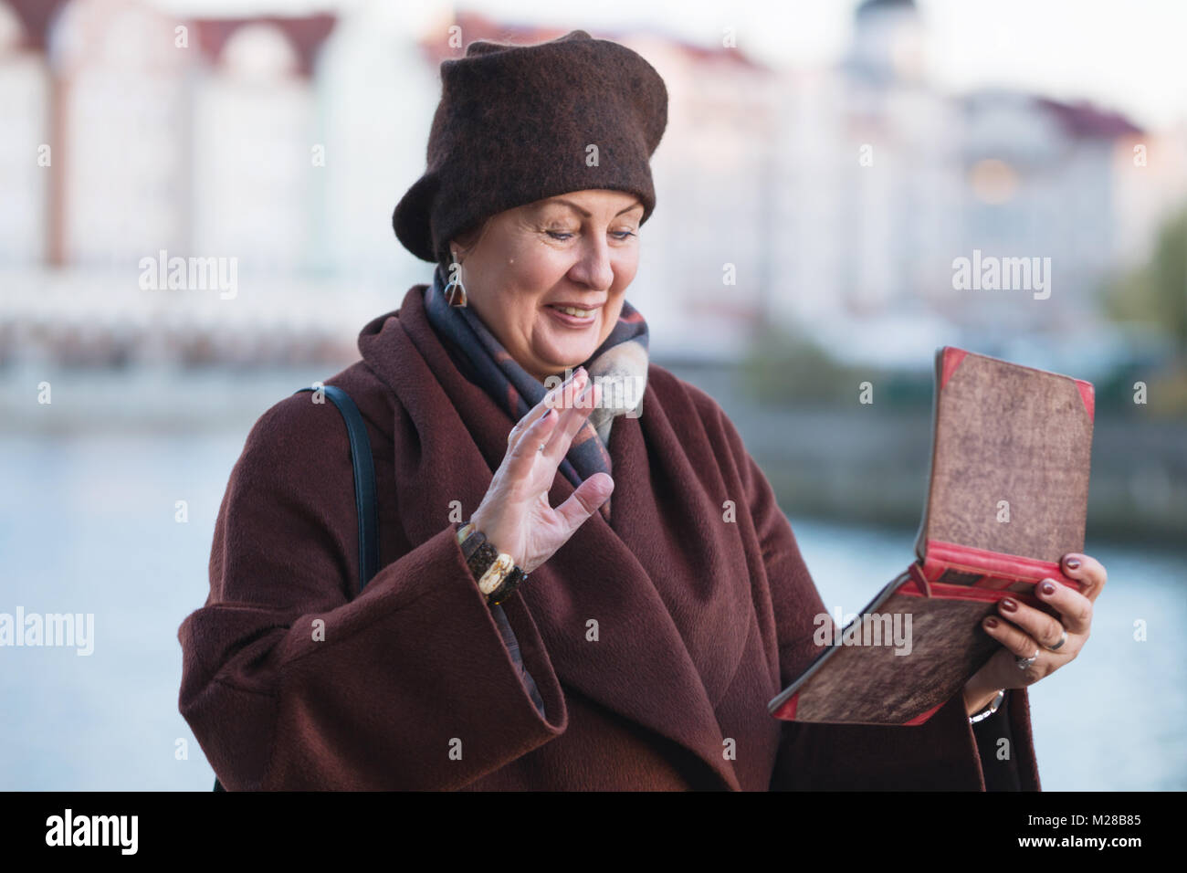 Una donna anziana in un cappotto marrone comunica tramite una tavoletta digitale Foto Stock