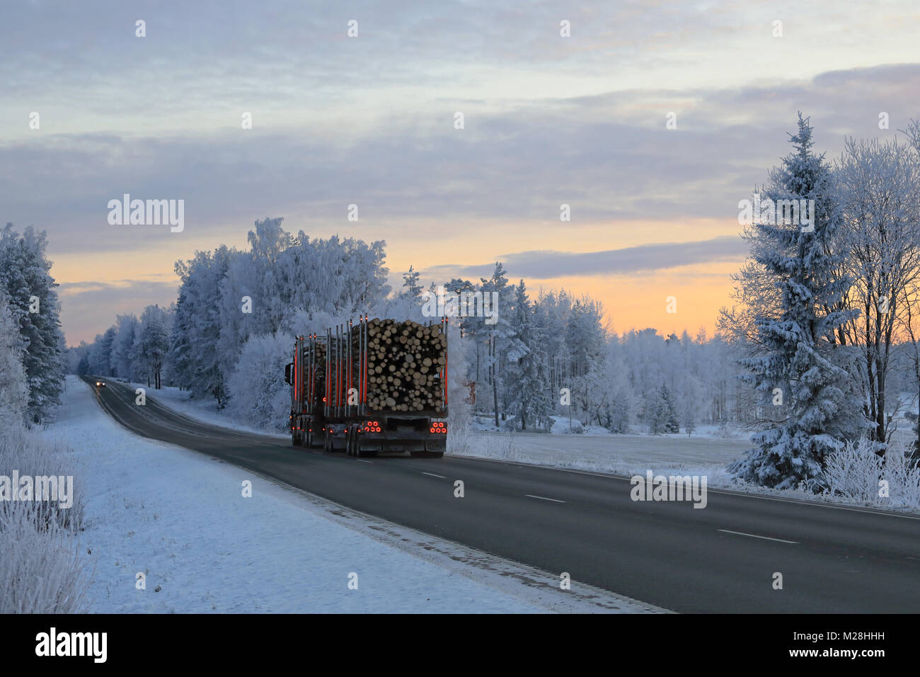 Paesaggio di una autostrada in inverno al tramonto con alberi smerigliato e carrello di registrazione che traina un pieno carico di legname. Foto Stock