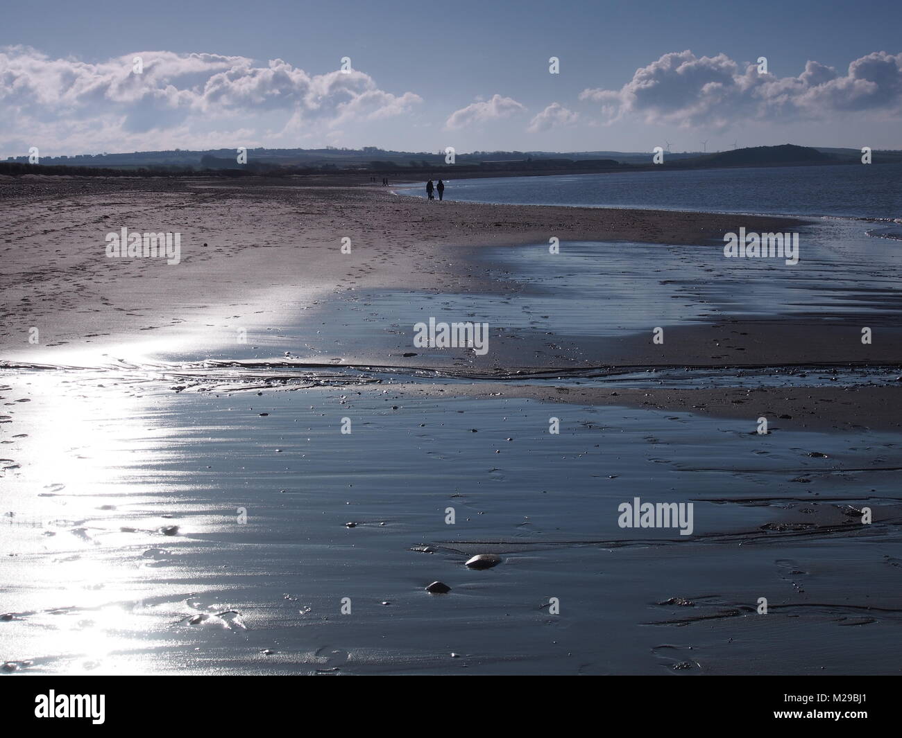 In inverno il sole scintillante sulla sabbia bagnata con il cane walkers a distanza, Allonby Beach, Solway Firth, Cumbria, Regno Unito Foto Stock