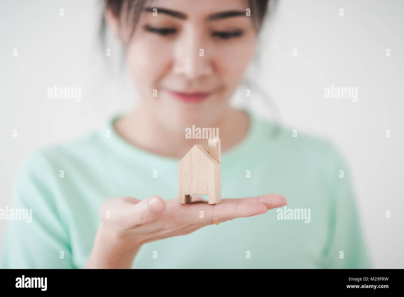 Attraente giovane donna asiatica che mostra piccola casa in legno modello nella sua mano. Business, vita crescita e piano da sogno per il concetto di famiglia Foto Stock