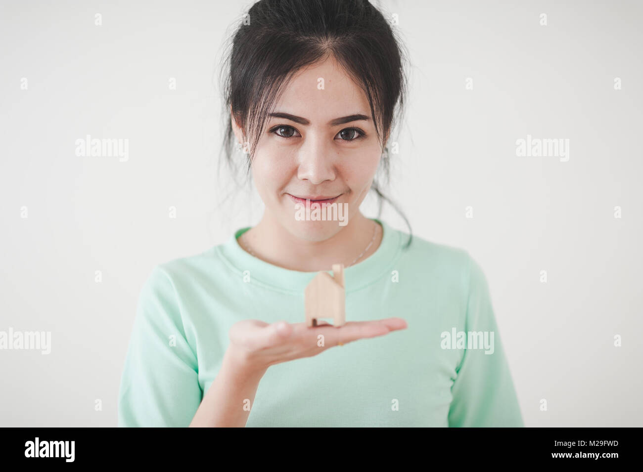 Attraente giovane donna asiatica che mostra piccola casa in legno modello nella sua mano. Business, vita crescita e piano da sogno per il concetto di famiglia Foto Stock
