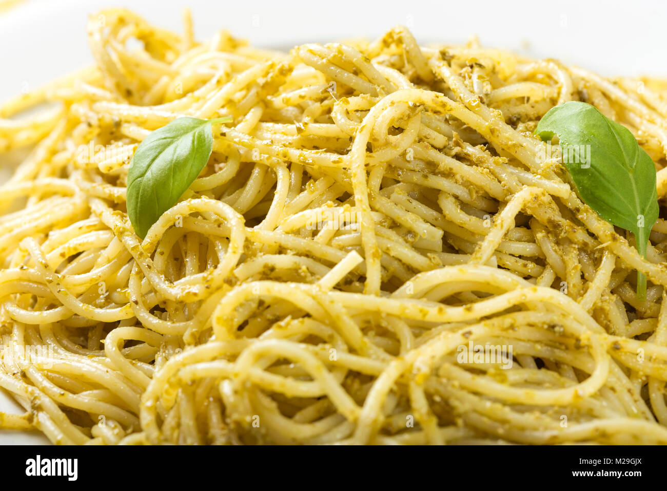 Close up di spaghetti fatti in casa con pesto di olio di oliva con le foglie di basilico sulla piastra bianca Foto Stock