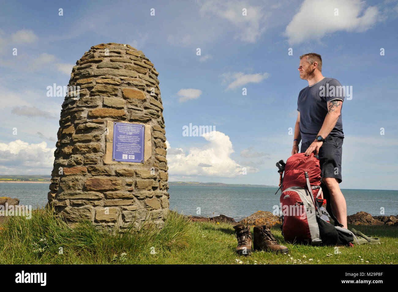 Un viandante si appoggia il suo i piedi stanchi presso la grande sfida all'aperto XXV anniversario cairn a Scurdie Ness luce Montrose, Angus, Scozia. Foto Stock