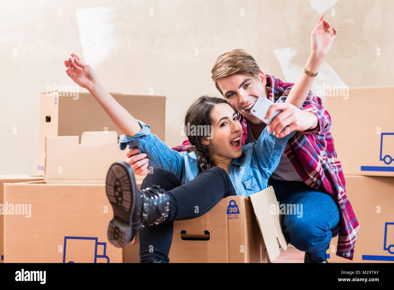 Felice giovane uomo e donna in posa mentre si effettua una selfie circondato dalle caselle dopo lo spostamento in una nuova casa Foto Stock