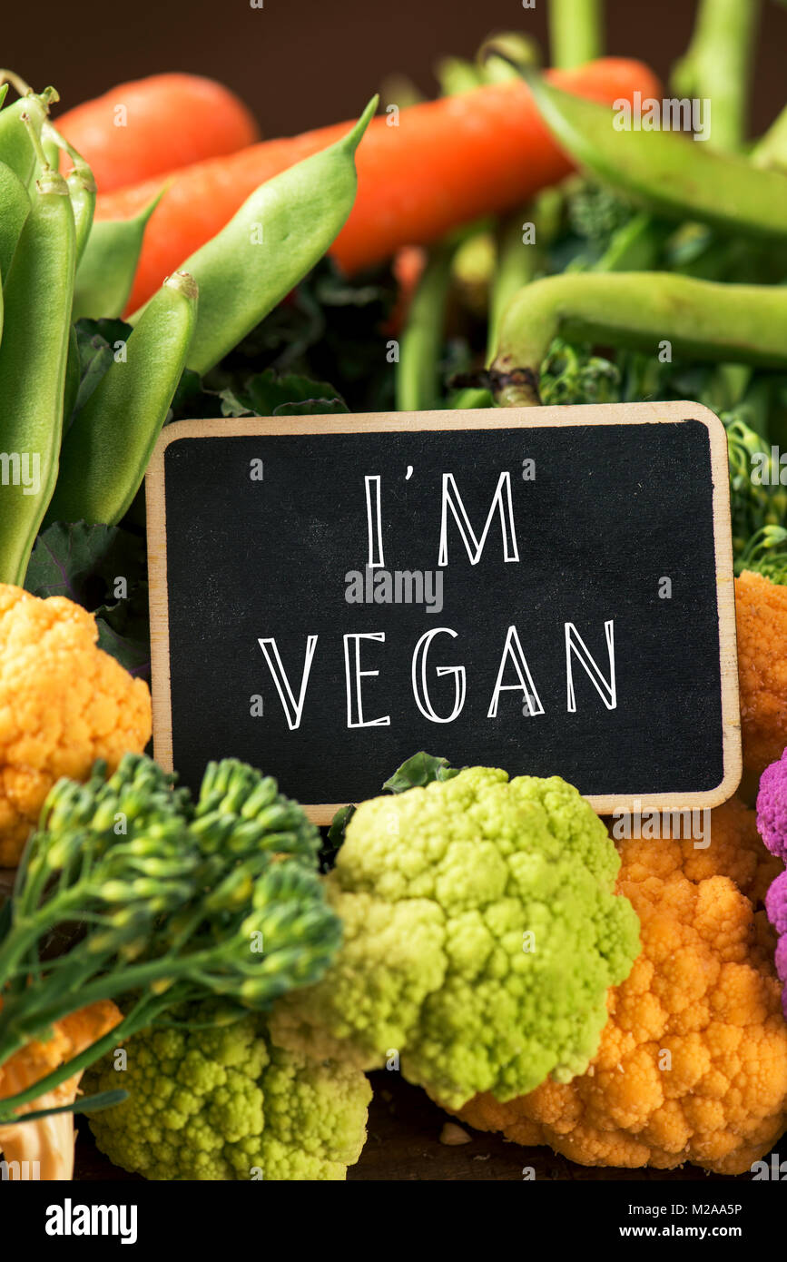 Primo piano di un cartello con scritto il testo io sono vegan collocato su una pila di alcune diverse verdure crude, come i cavolfiori di diversi colori, broccolini Foto Stock