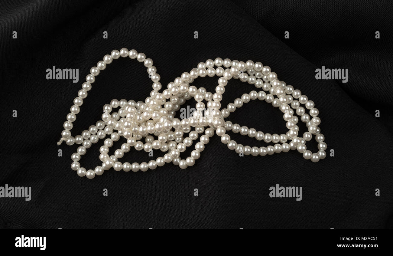 Una stringa di vecchi fake perle su un tessuto nero lo sfondo. Foto Stock