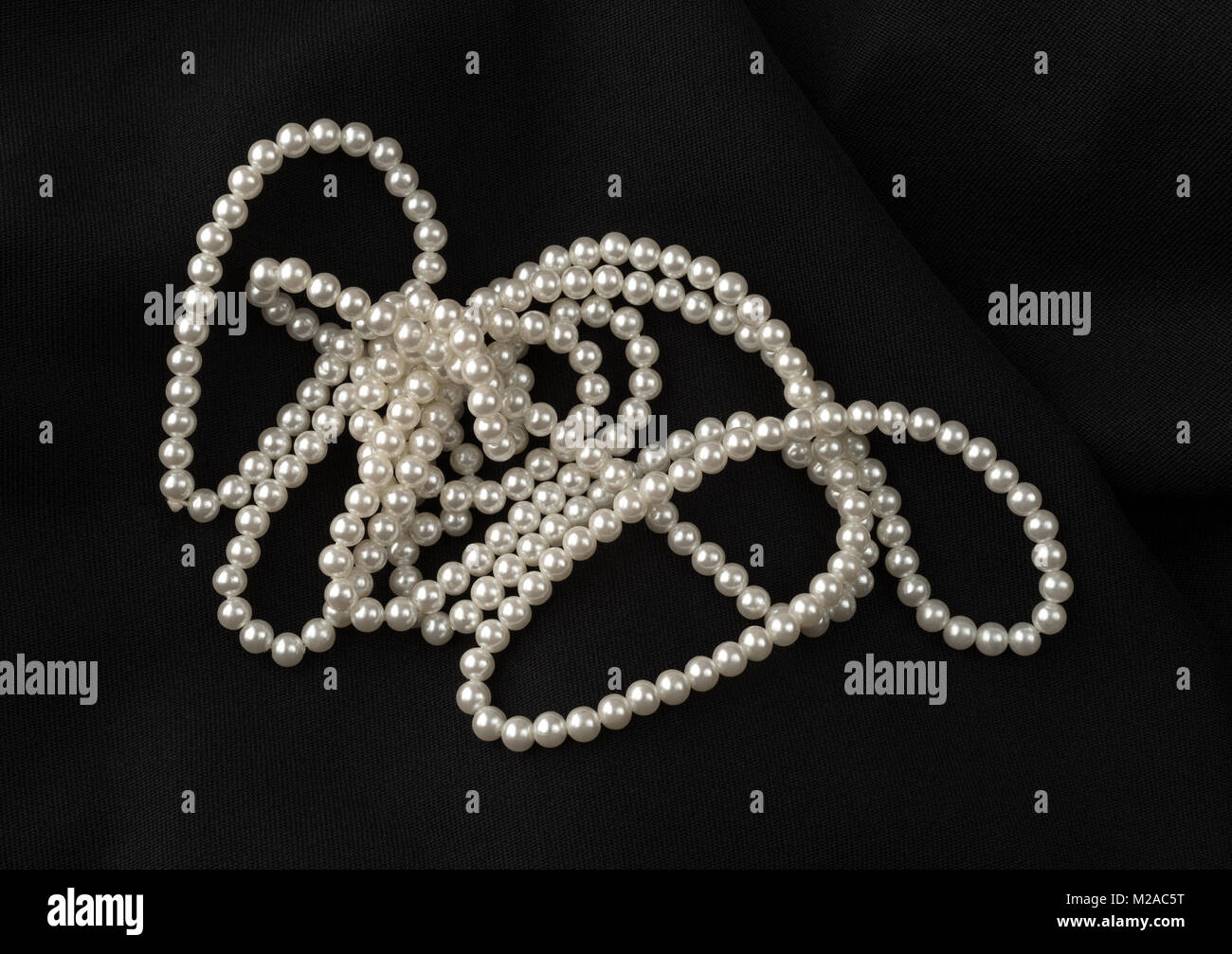 Una stringa di vecchi fake perle su un tessuto nero lo sfondo. Foto Stock
