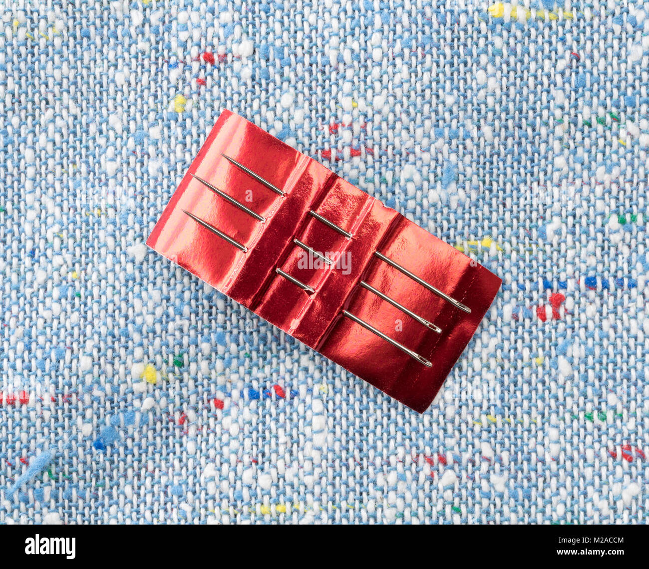 Regolare gli aghi da cucire in rosso gli imballaggi di carta in cima a un panno colorato sfondo. Foto Stock