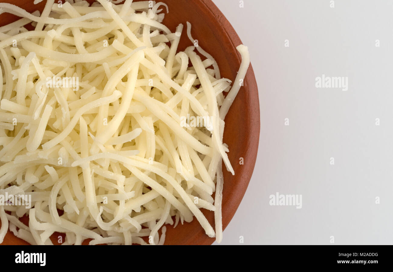 Top vista ravvicinata di una piccola ciotola riempita con finemente tritati sharp di formaggio cheddar bianco in cima al tavolo bianco. Foto Stock