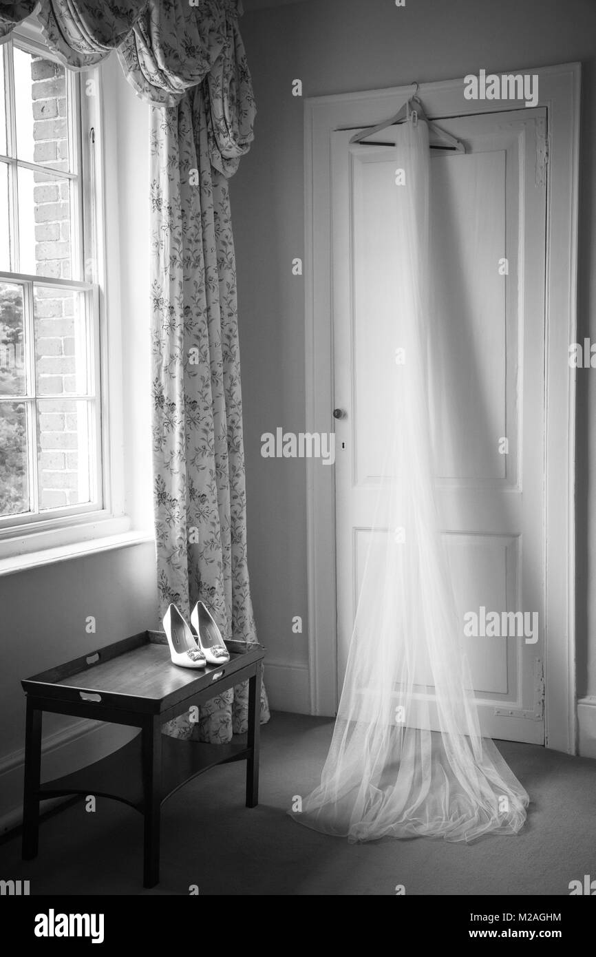 Velo di nozze appeso sulla porta e scarpe sulla tavola, in bianco e nero Foto Stock