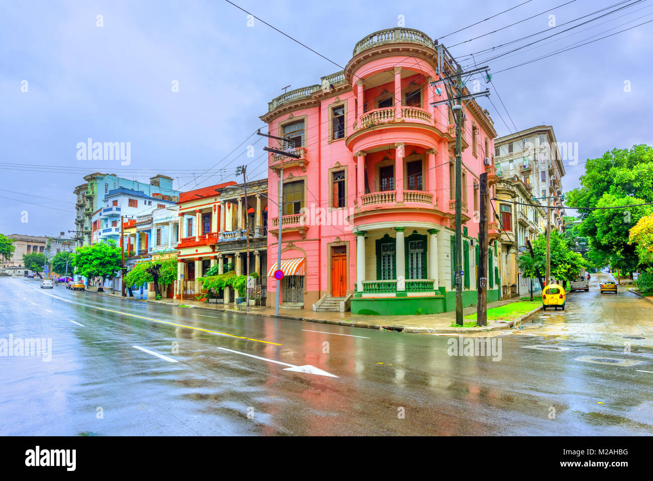 Antica multi-edifici colorati con colonne sulla strada di Havana cubana a mezzogiorno dopo la pioggia, asfalto e cielo blu Foto Stock