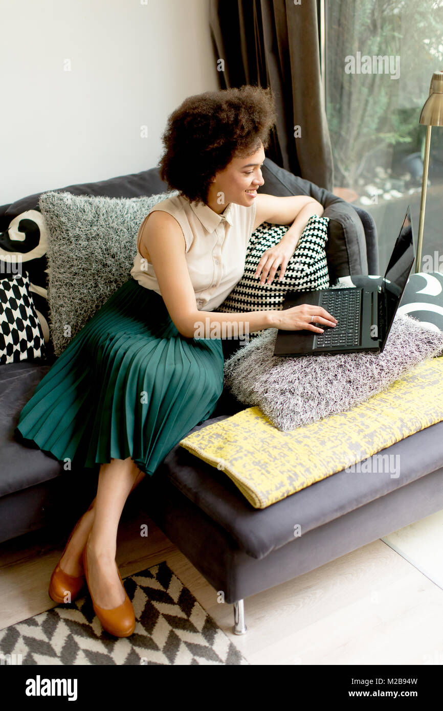 Giovane africano donna americana con computer portatile seduto in salotto luminoso a casa Foto Stock