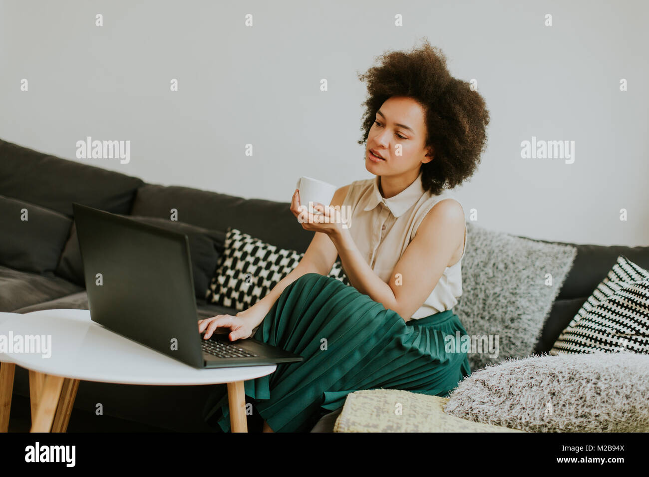 Giovane africano donna americana con computer portatile seduto in salotto luminoso a casa Foto Stock