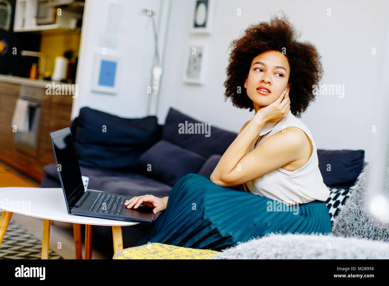 Giovane africano donna americana con computer portatile seduto in salotto luminoso a casa Foto Stock