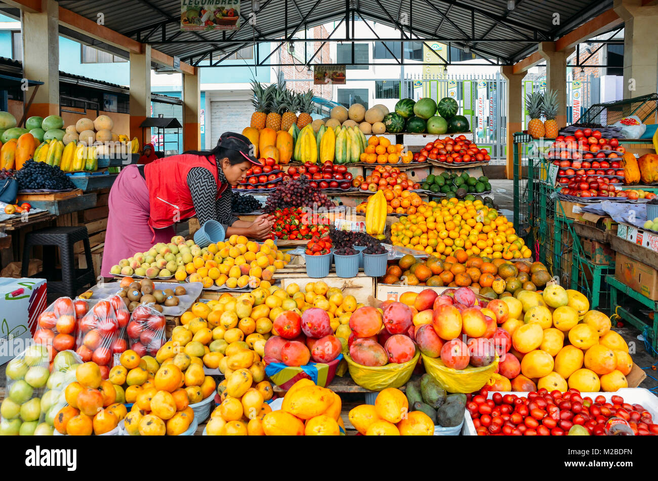 Ambato, Ecuador, Dicembre 20, 2017: donna ecuadoriana fruttivendola di fronte a lei visualizza di frutti tropicali in un mercato Foto Stock