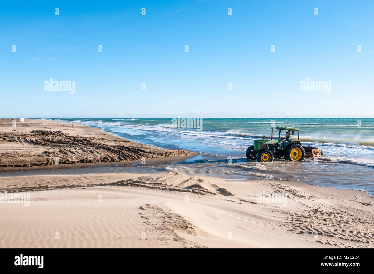 Il trattore trainato beach cleaner rastrellando sabbia di mare, lavorando sulla spiaggia, il delta del fiume Ebro, Catalogna, Spagna Foto Stock