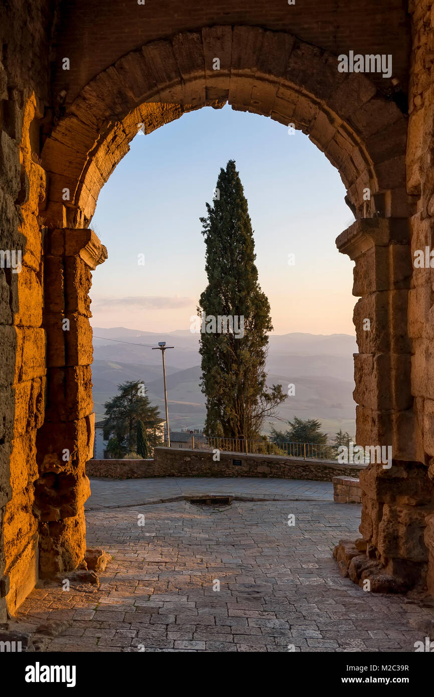 Cipresso incorniciato dalla porta all'arco porta, Volterra, Pisa, Toscana, Italia Foto Stock