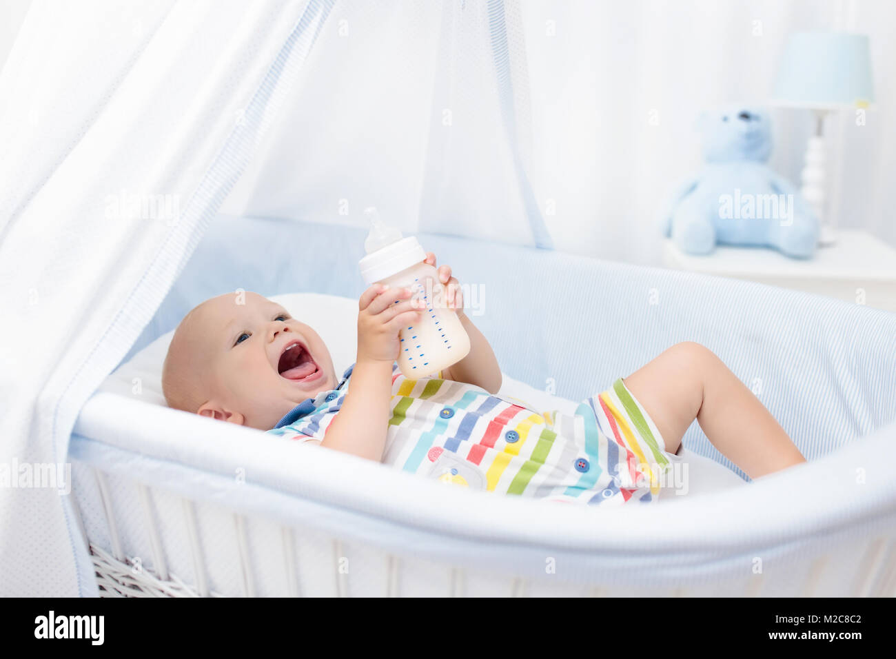 Baby bere latte in bianco presepe. Ragazzo per neonati con formula bottiglia in letto. I ragazzi di nutrizione. Cibo sano e bevande per bambini. Bambino in bianco vivaio. Foto Stock