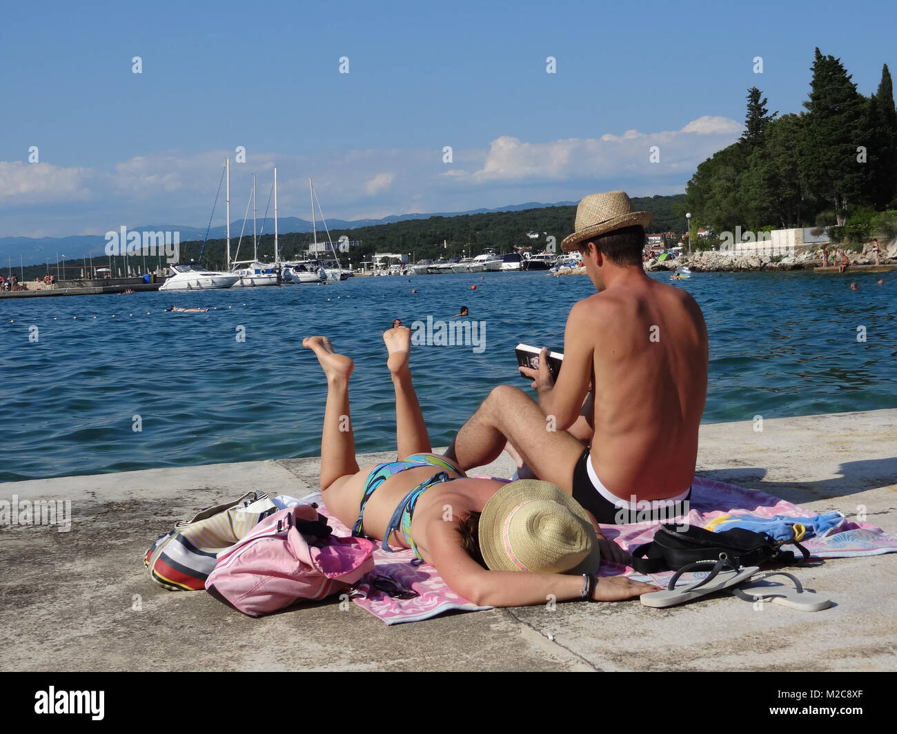 Die Füße hoch legen, Sommer, Sonne und mehr - die Urlauber freuen sich auf die schönsten Zeit des Jahres. Eine Frau liest ein Buch und telefoniert am Strand. Telefonieren in der EU ist seit dem 1. Juli 2013 billiger. Ein Mann und eine Frau finden Entspannung. Foto Stock