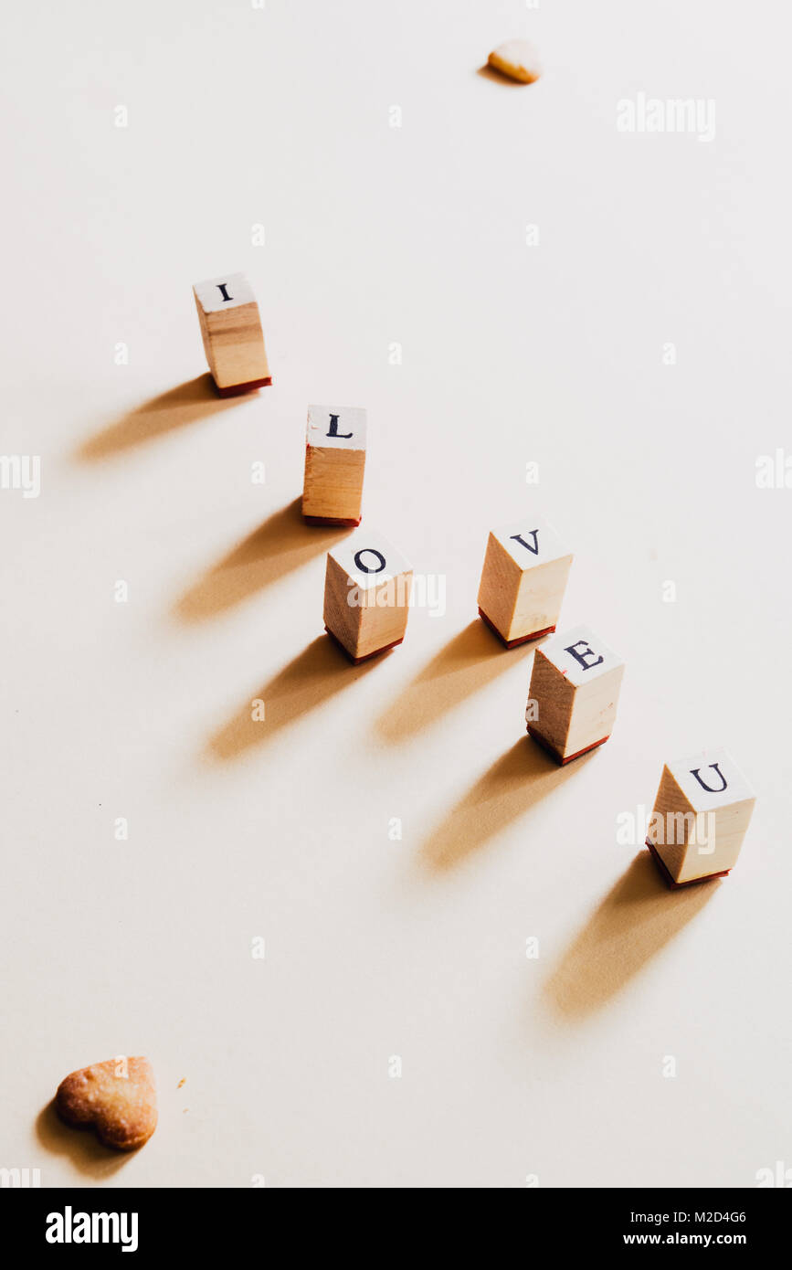 Lettera timbro formando la frase ' i love u' contro un pastello giallo sfondo per il giorno di san valentino giorno, vista dall'alto. Foto Stock