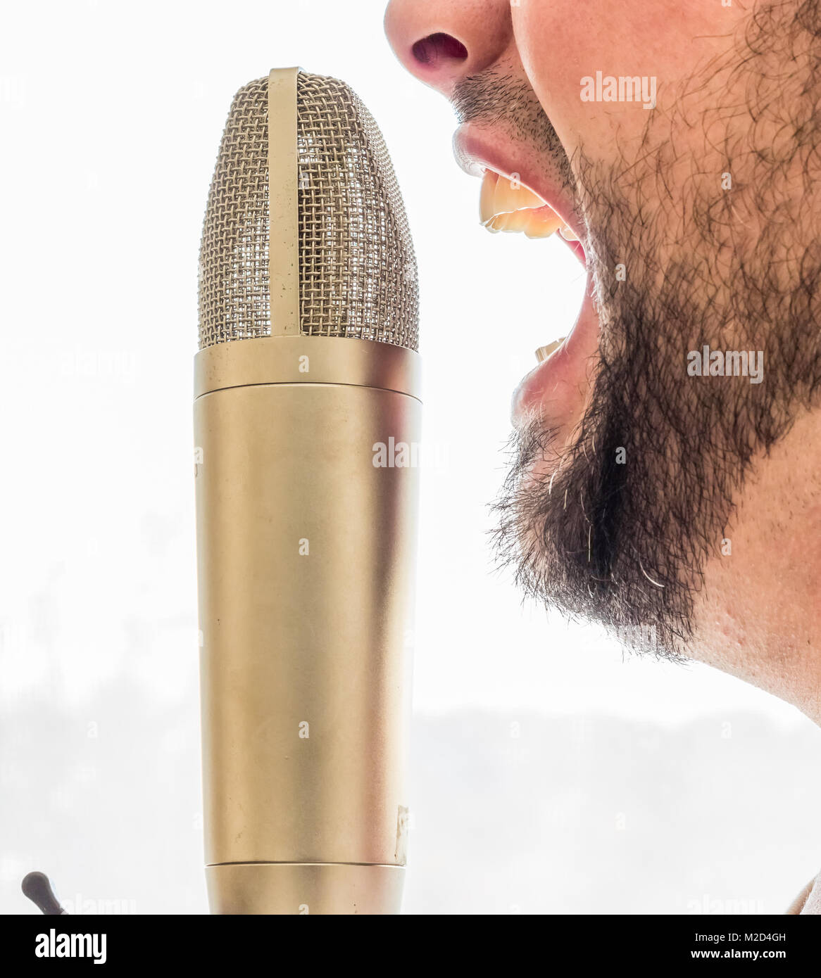 Un vecchio gold microfono è impostato nella parte anteriore di una faccia di sesso maschile. Il maschio è urlando nel microfono. Lo sfondo è tutto bianco. Foto Stock