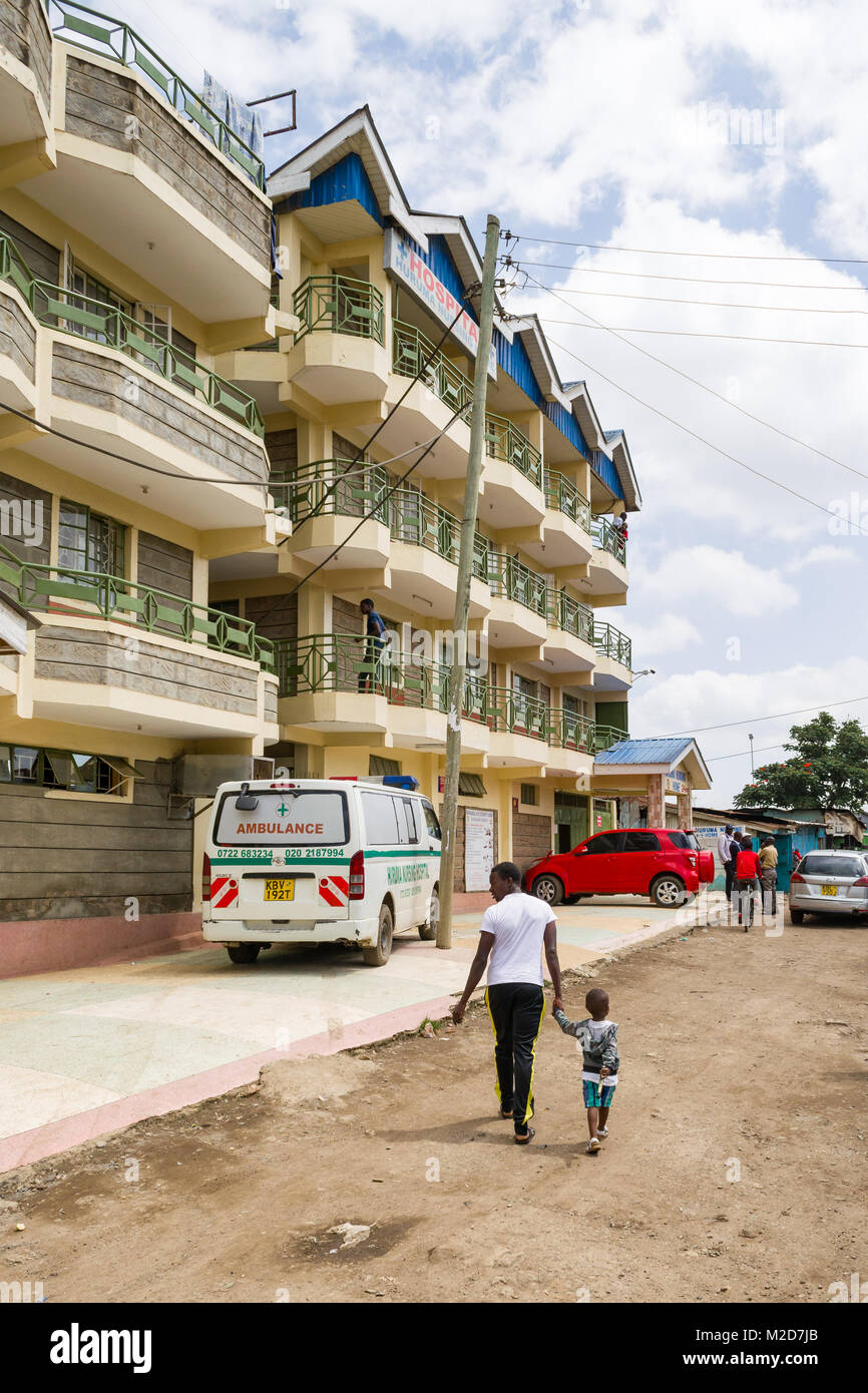 La parte esterna di un ospedale a Huruma con gente camminare passato su un polveroso sentiero di grandi dimensioni, Nairobi, Kenia Foto Stock