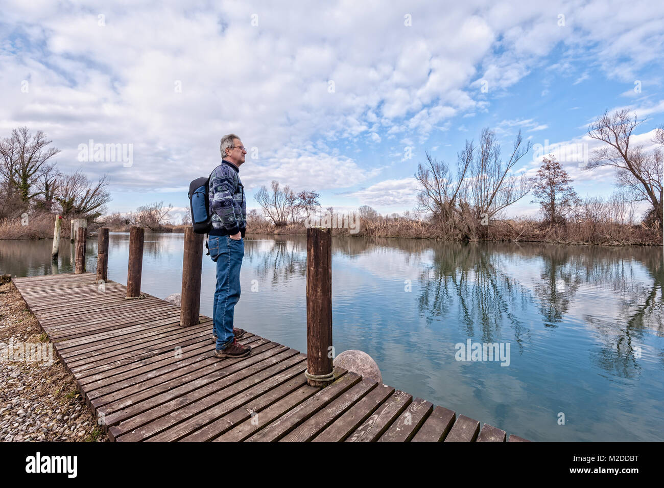 La natura del paesaggio. Escursionista senior con zaino oltre il molo di legno sulla riva del fiume. Foto Stock
