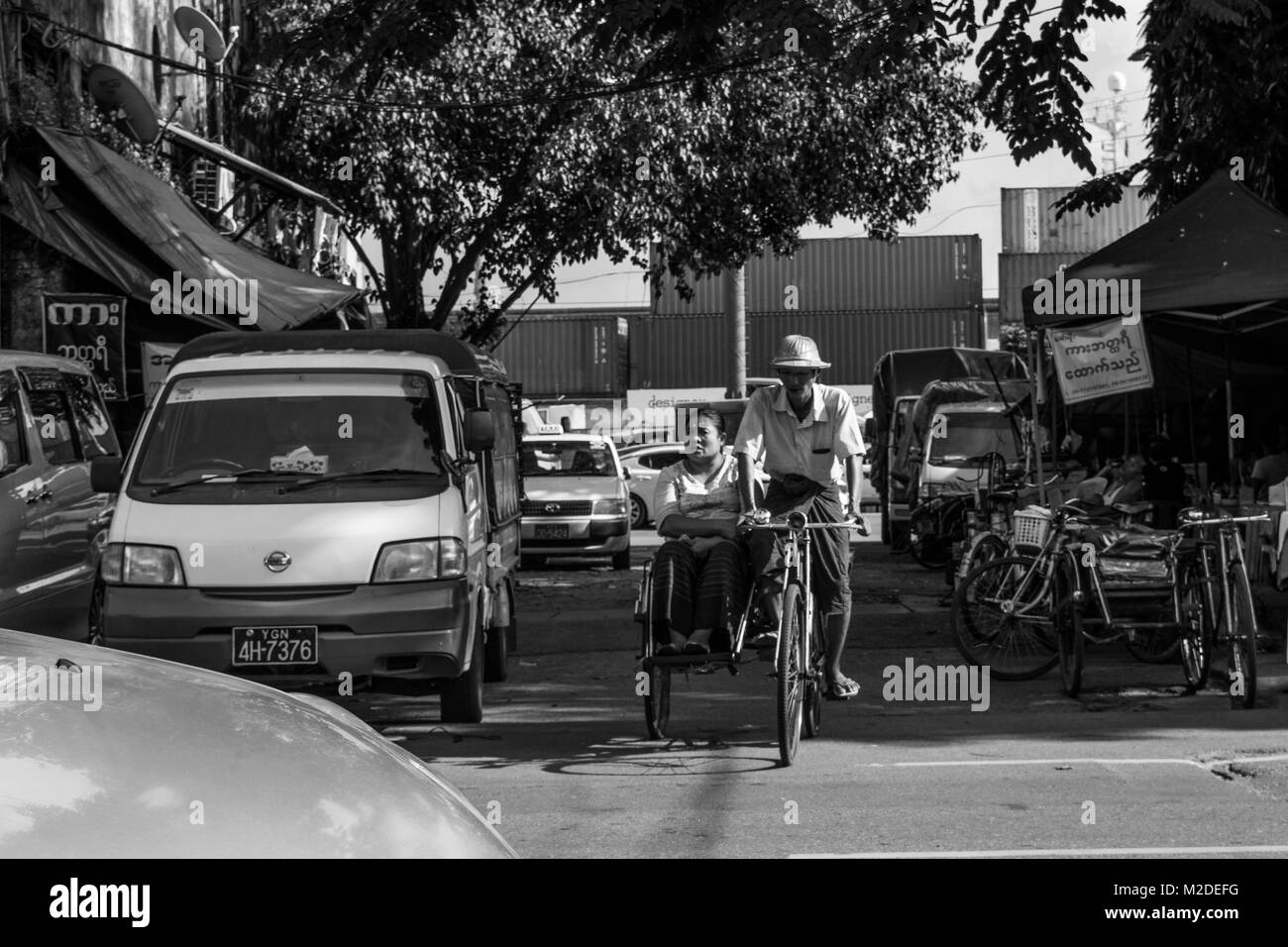 Un giovane birmano, eventualmente il marito e la moglie, con l'uomo alla guida di un ciclo rickshaw nel frenetico traffico di Yangon e la moglie seduta passeggero. Myanmar Foto Stock