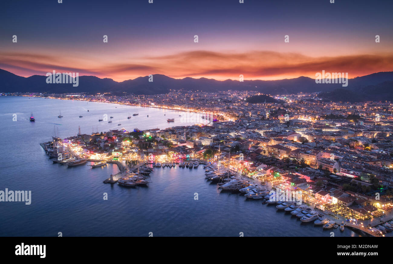 Vista aerea di barche e bella città di notte a Marmaris, Turchia. Paesaggio con barche in Marina Bay, il mare, le luci della città, montagne, red sky e nuvole Foto Stock