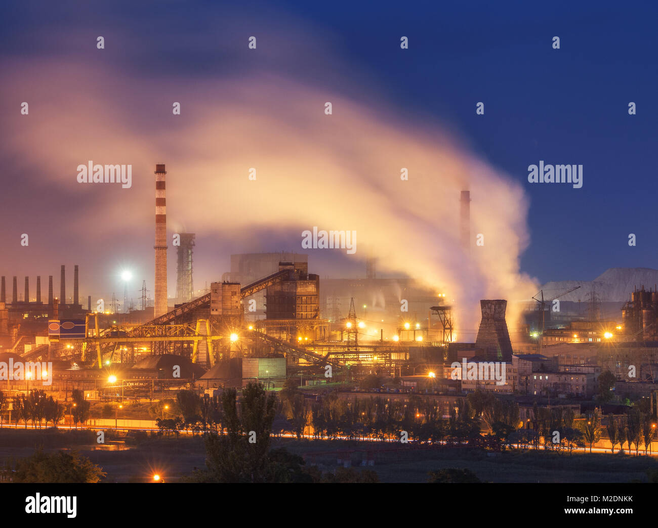 Stabilimento metallurgico di notte. Fabbrica di acciaio con fumaioli. Acciaierie e lavori di ferro. Industria pesante in Europa. Inquinamento atmosferico da fumaioli ecolog Foto Stock