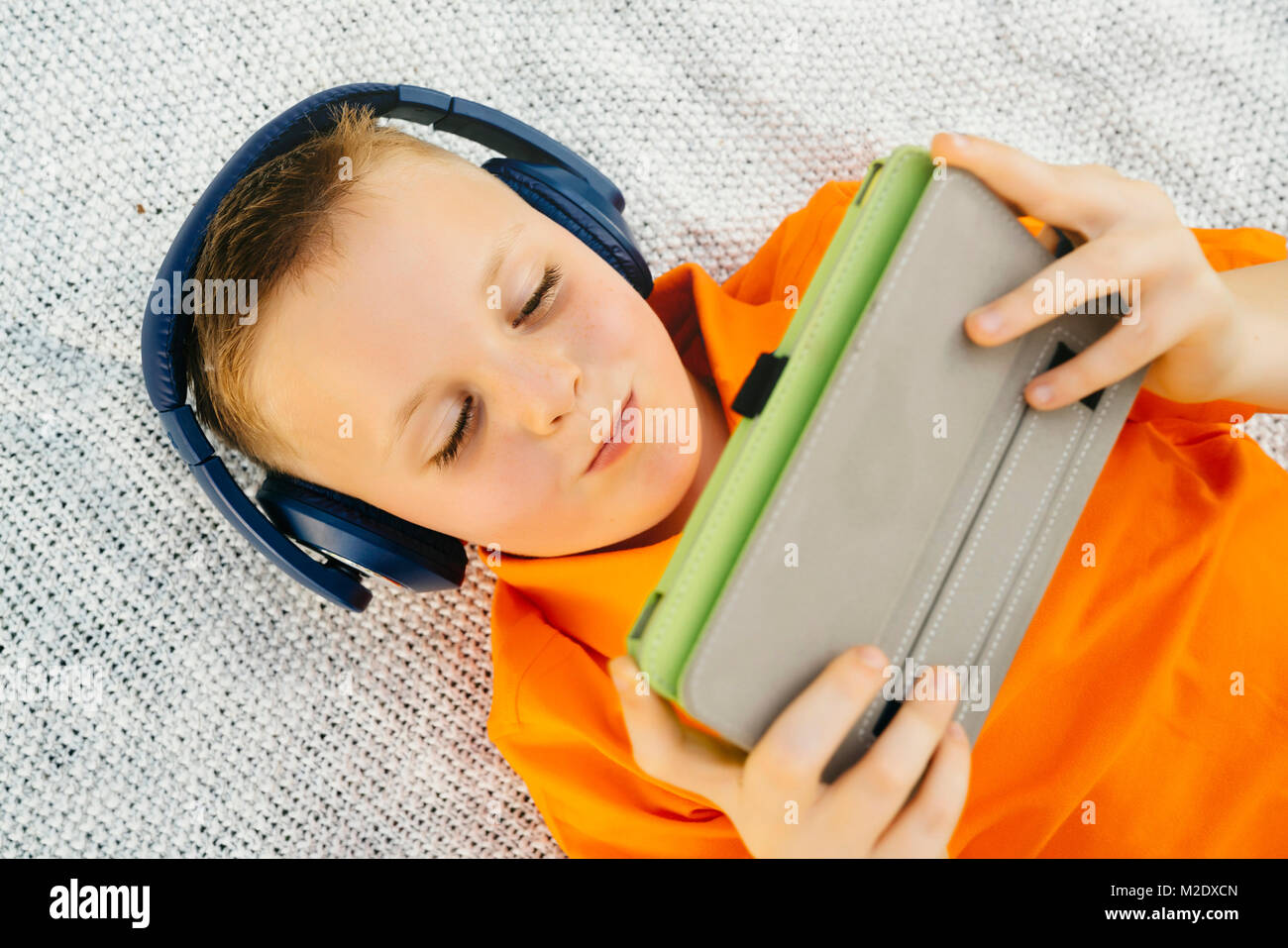 Sorridente ragazzo caucasico posa sulla coperta di ascolto digitale compressa Foto Stock