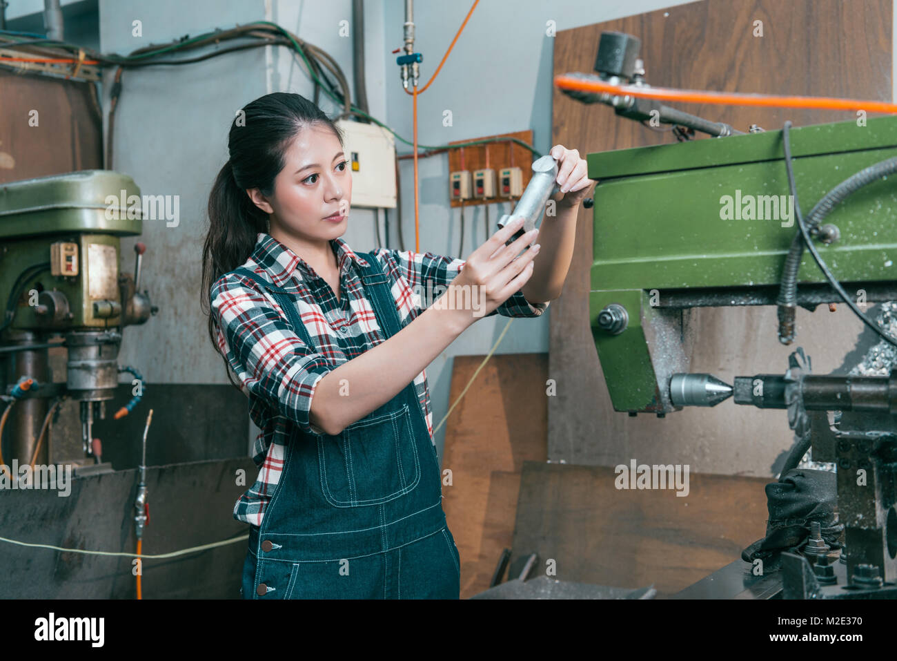 Professional piuttosto di lavorazione a tornio donna di fabbrica lavoratore confermare i componenti in ambiente di lavoro quando si è finito di fresatura il lavoro di elaborazione. Foto Stock