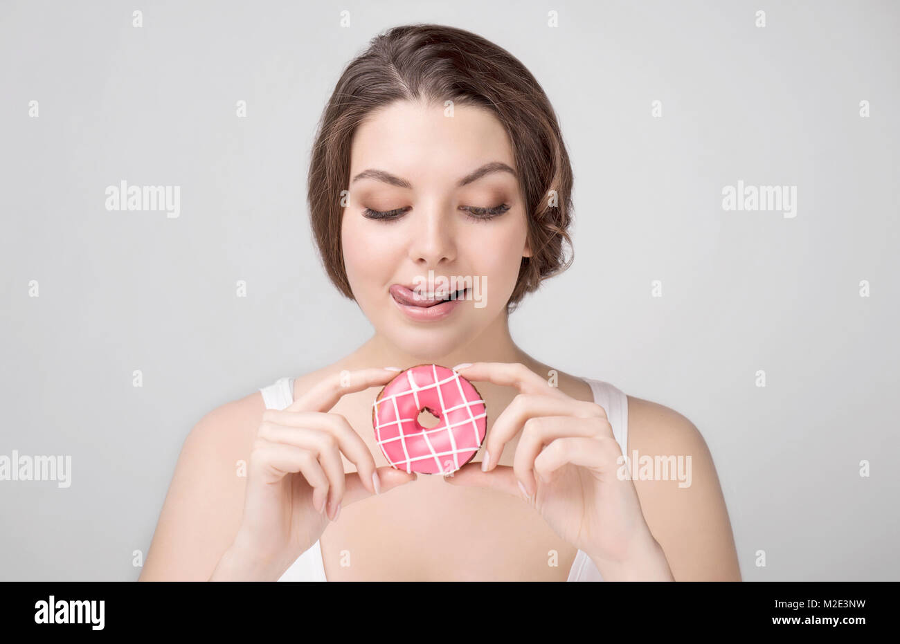 La donna caucasica tenendo a ciambella e leccarsi le labbra Foto Stock