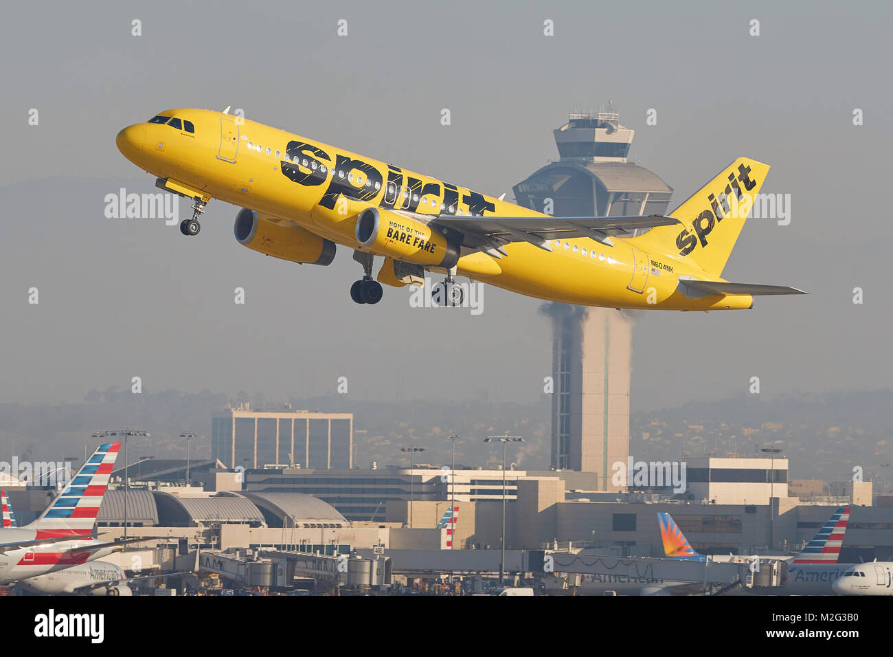 Spirito alle compagnie aeree di colore giallo brillante Airbus A320 di decollo dall'Aeroporto Internazionale di Los Angeles, il sistema di controllo del traffico aereo torre in background. Foto Stock