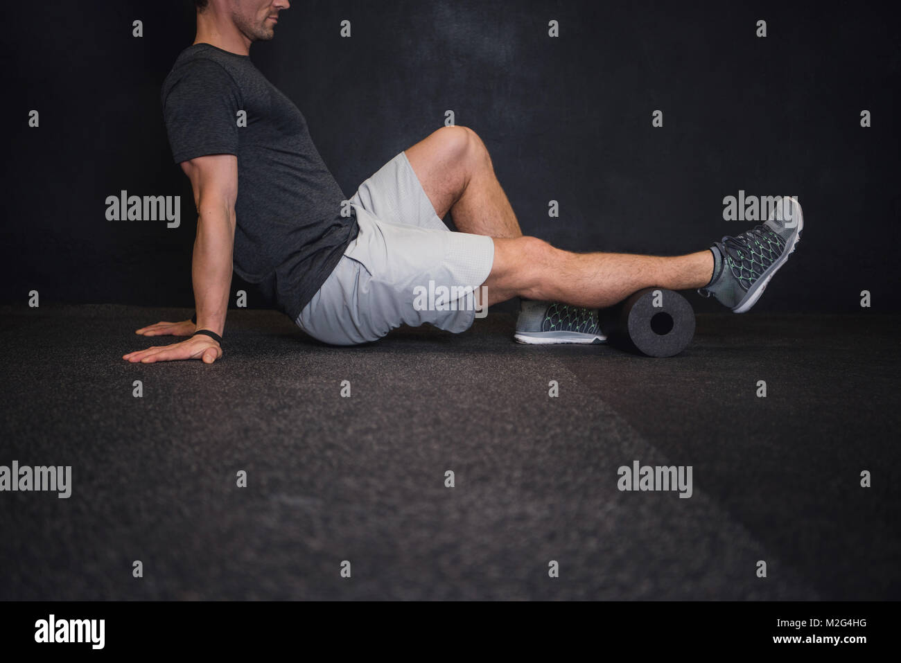 Athletic uomo usando un rullo in gomma spugna per alleviare muscoli doloranti dopo un allenamento. Foto Stock