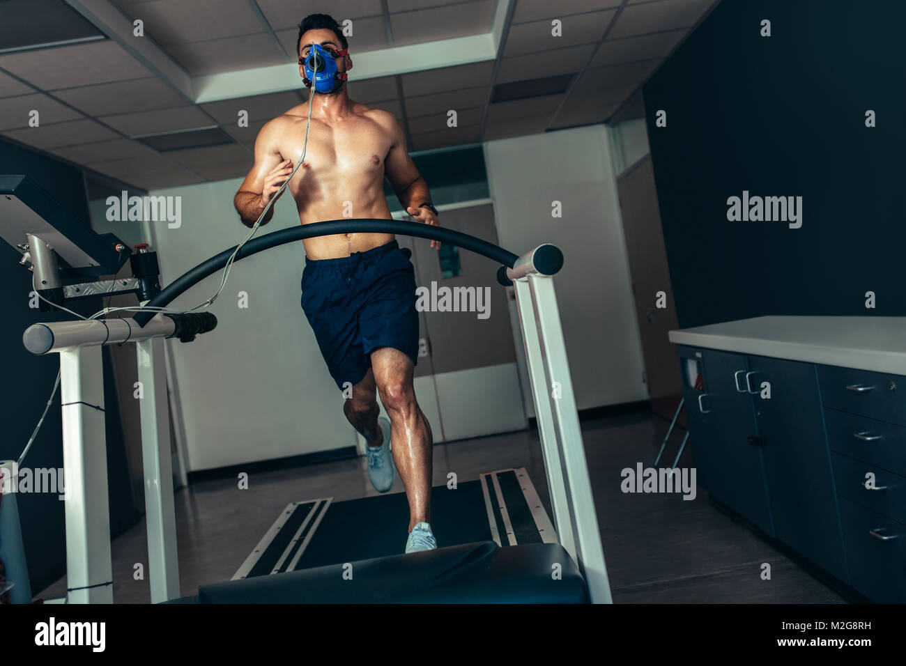 Atleta maschio esaminando il suo fitness sport in laboratorio. Runner con maschera facendo una prova delle prestazioni sul tapis roulant. Foto Stock
