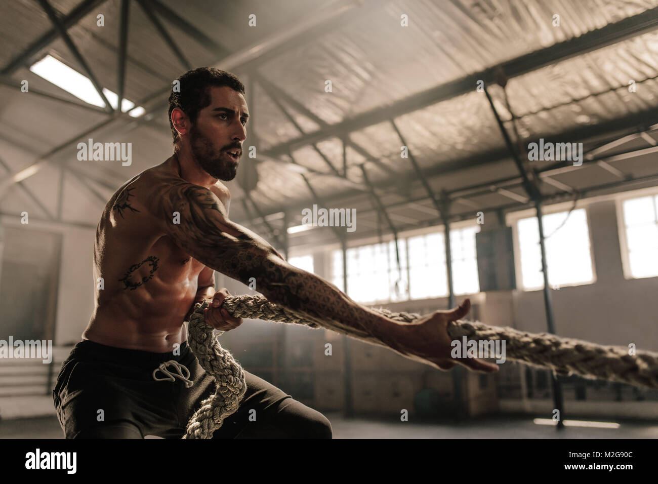 Uomo forte il traino di pesanti corda in cross training gym. Atleta maschio a fare gli esercizi con la corda in palestra. Foto Stock