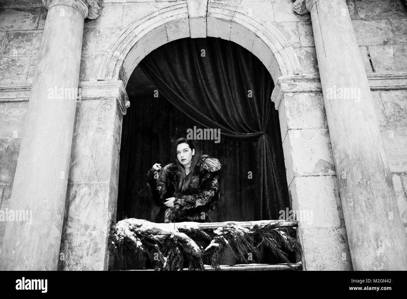 Bruna ragazza in verde pelliccia contro il vecchio arco con colonne e tendaggi rossi. Foto Stock