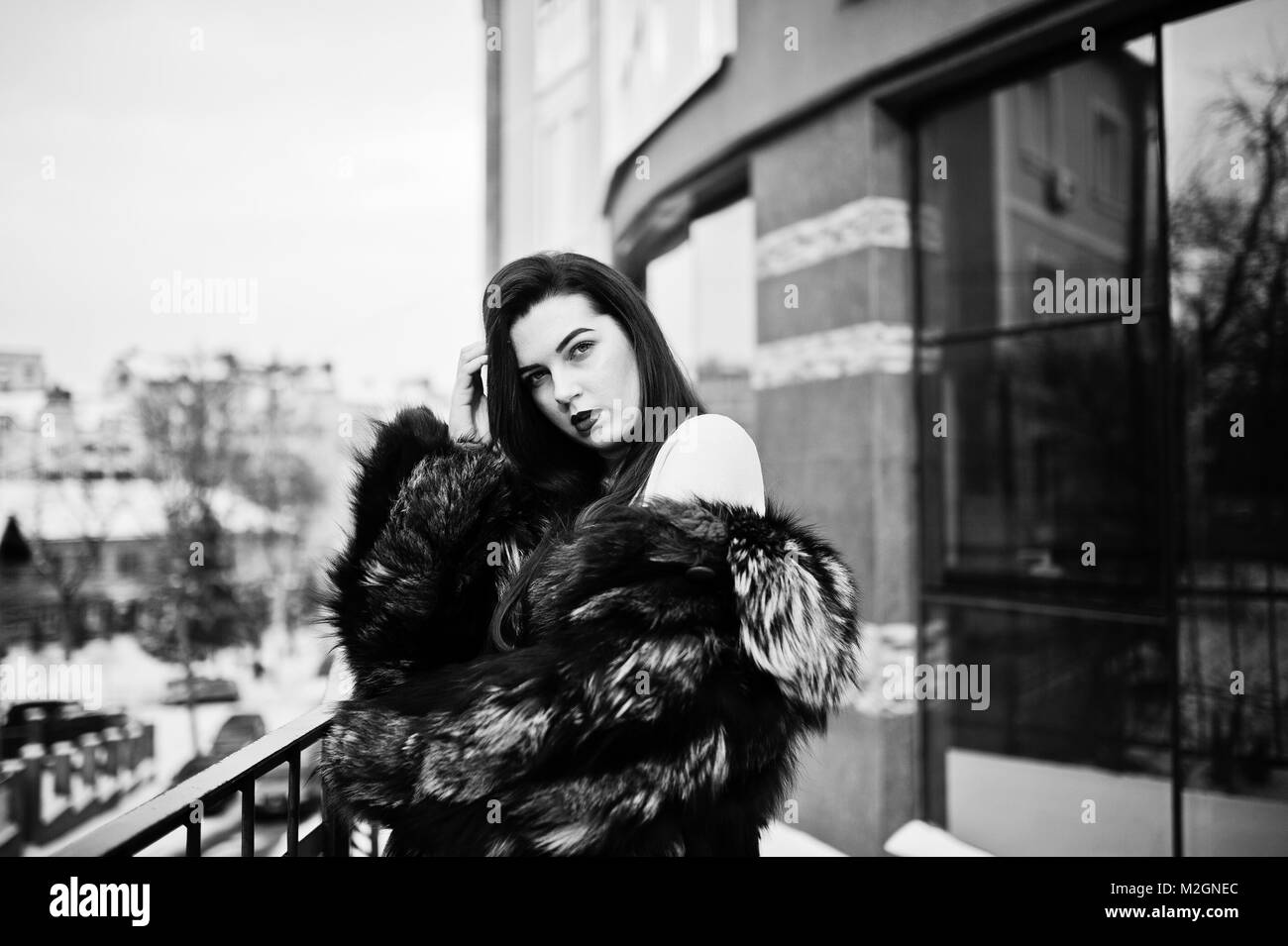 Bruna ragazza in verde pelliccia lungo la strada della città contro la casa con grandi finestre presso l'inverno. Foto Stock