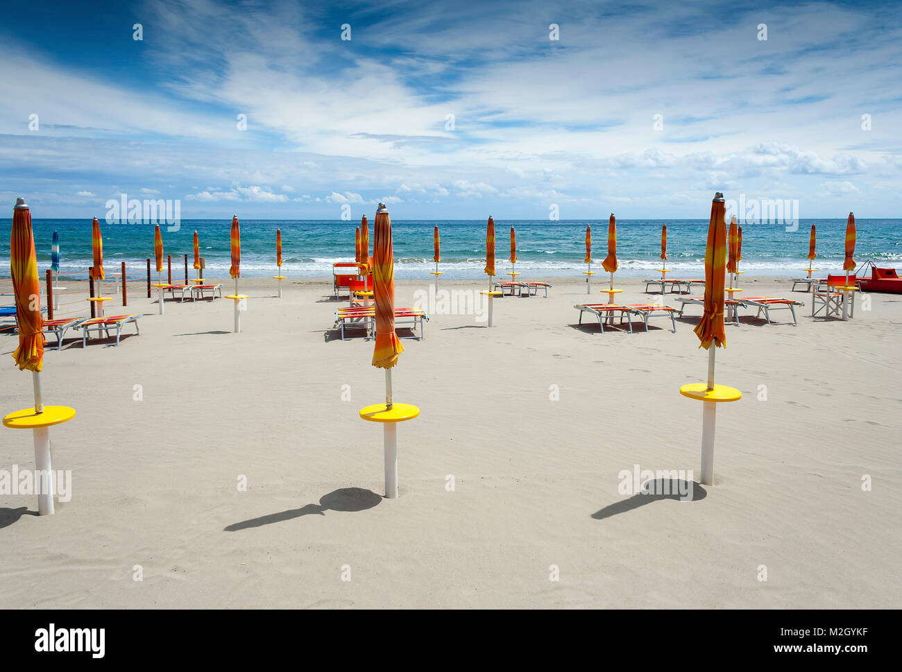 Laigueglia spiaggia sabbiosa al mattino prima che le persone sono arrivati ripiegato con ombrelloni e lettini per prendere il sole con un cielo blu e nuvole bianche in Liguria Italia Foto Stock