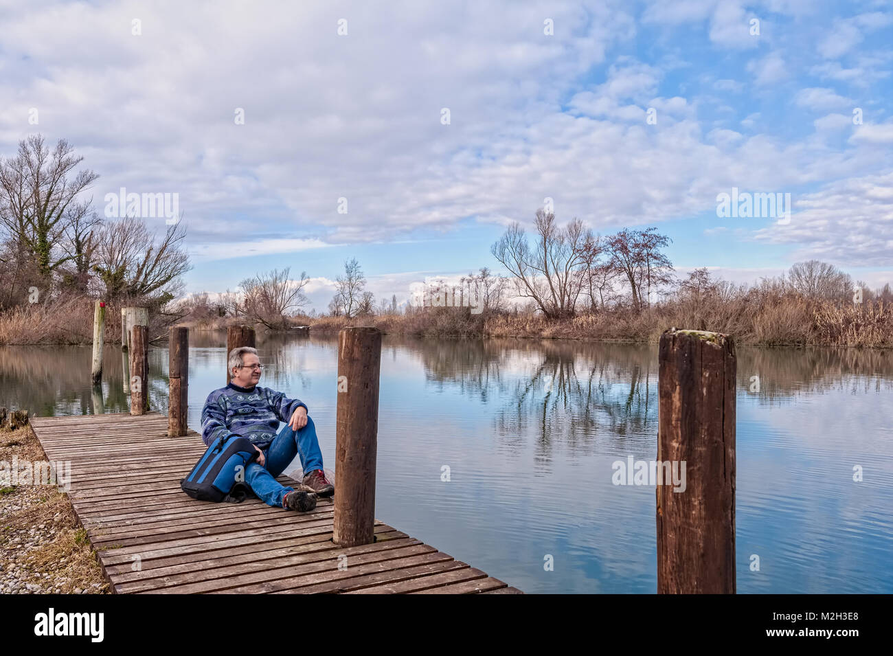 La natura del paesaggio. Escursionista senior con zaino oltre il molo di legno sulla riva del fiume. Foto Stock