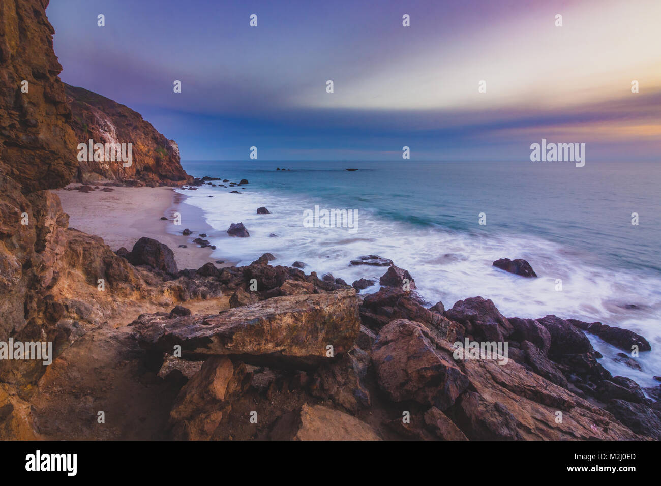 Appartata Pirate's Cove Beach al tramonto con un cielo colorato e l'acqua dell'oceano che scorre attorno a formazioni rocciose, Point Dume, Malibu, California Foto Stock