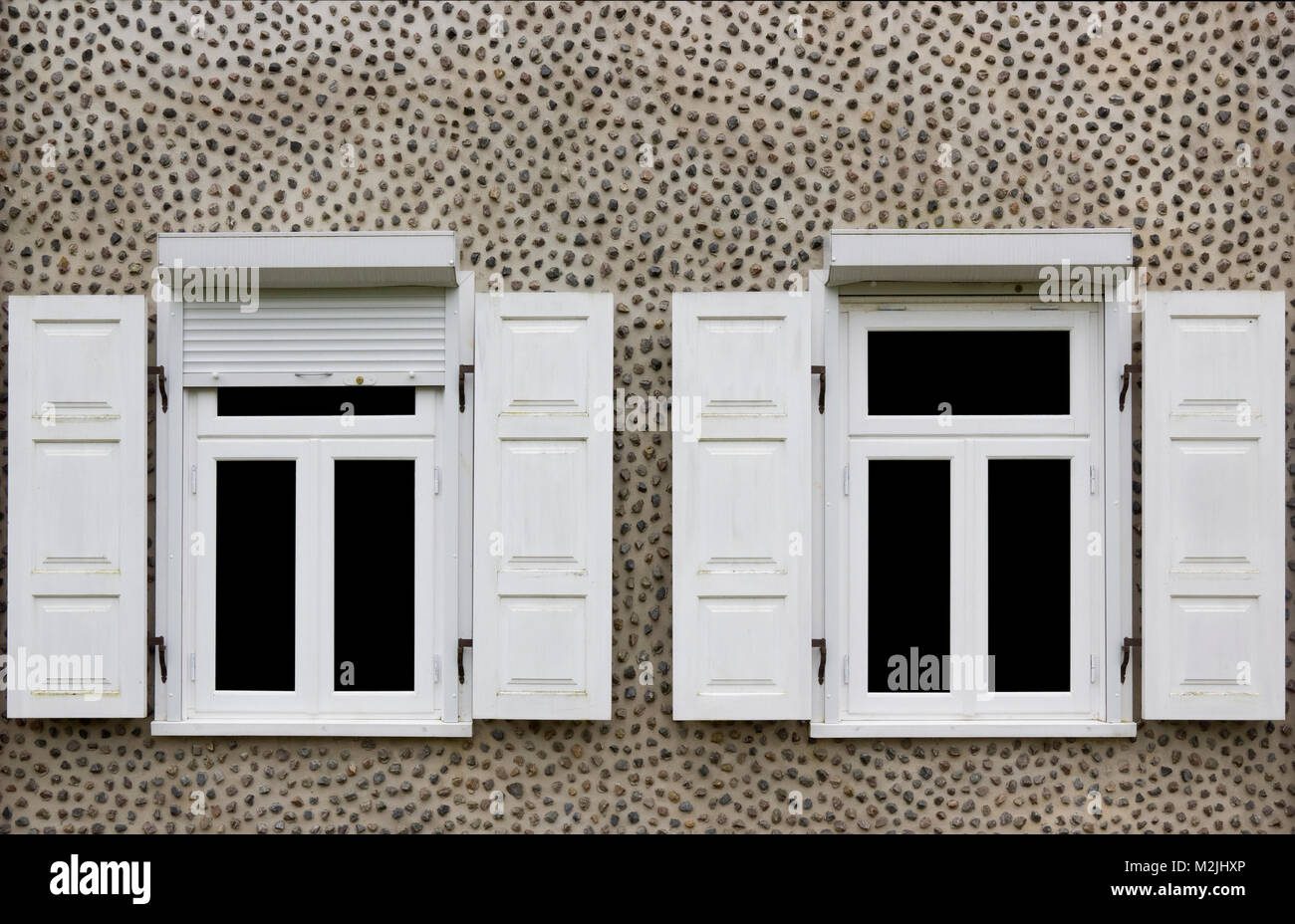 Due bianchi di nuove finestre con persiane aperte. Parete di casa decorata con piccole pietre di granito. Vetro isolato su nero Foto Stock