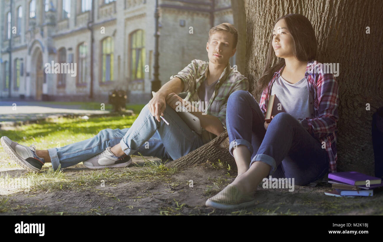 Multirazziale studenti maschi e femmine seduto sotto agli alberi, guardando al futuro, il futuro Foto Stock