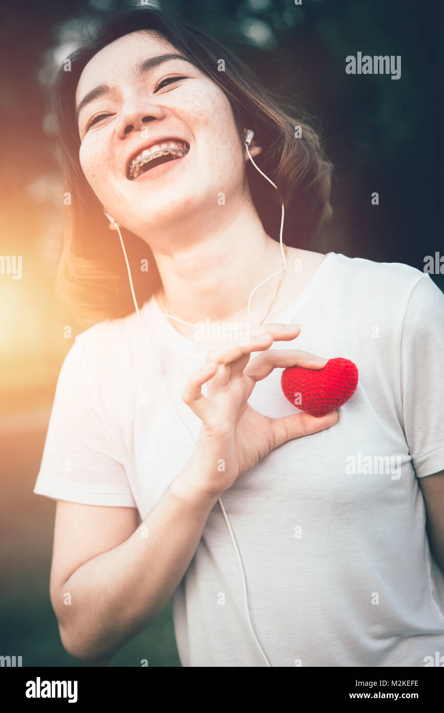 Ragazza adolescente sorriso con amore cuore ascoltando musica godere al momento con il sole Foto Stock